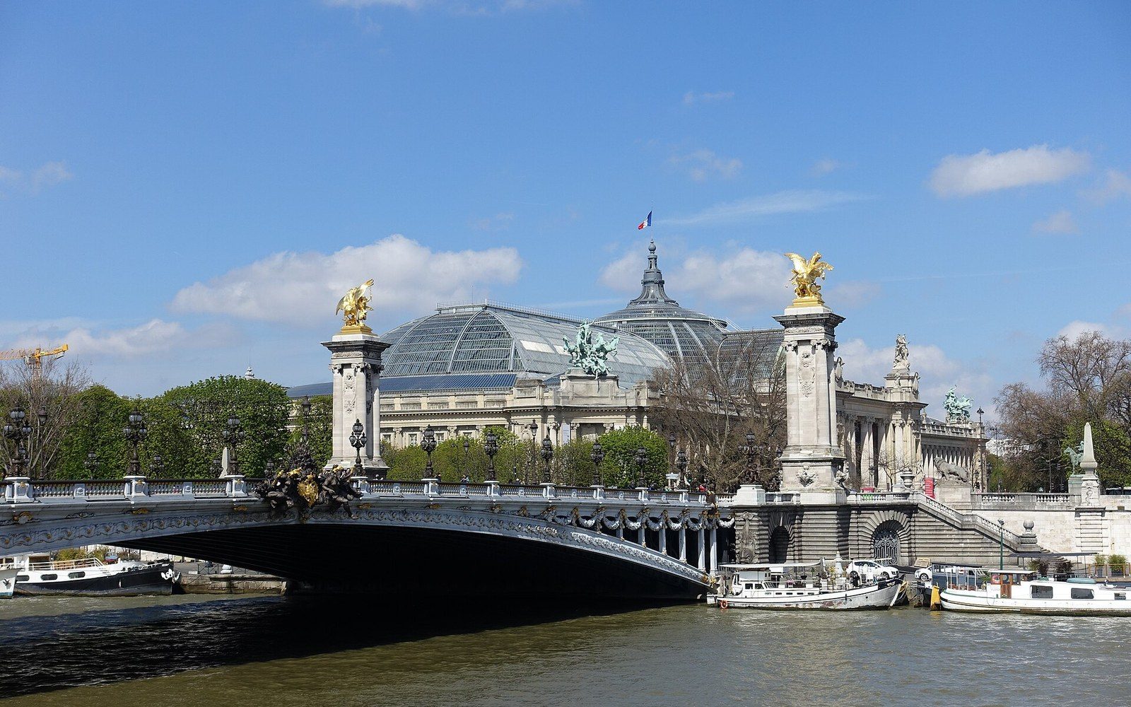 Ornate bridge with gilded statues spans the Seine before the glass-domed Grand Palais
